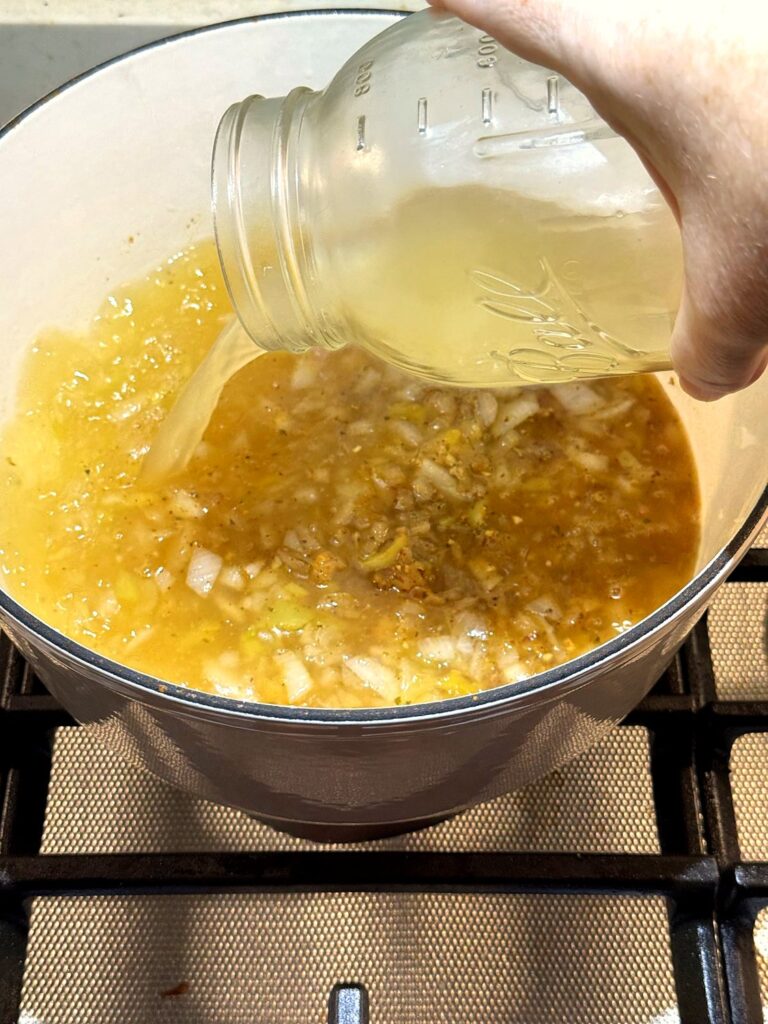 Chicken broth being poured from a glass jar into the Dutch oven
