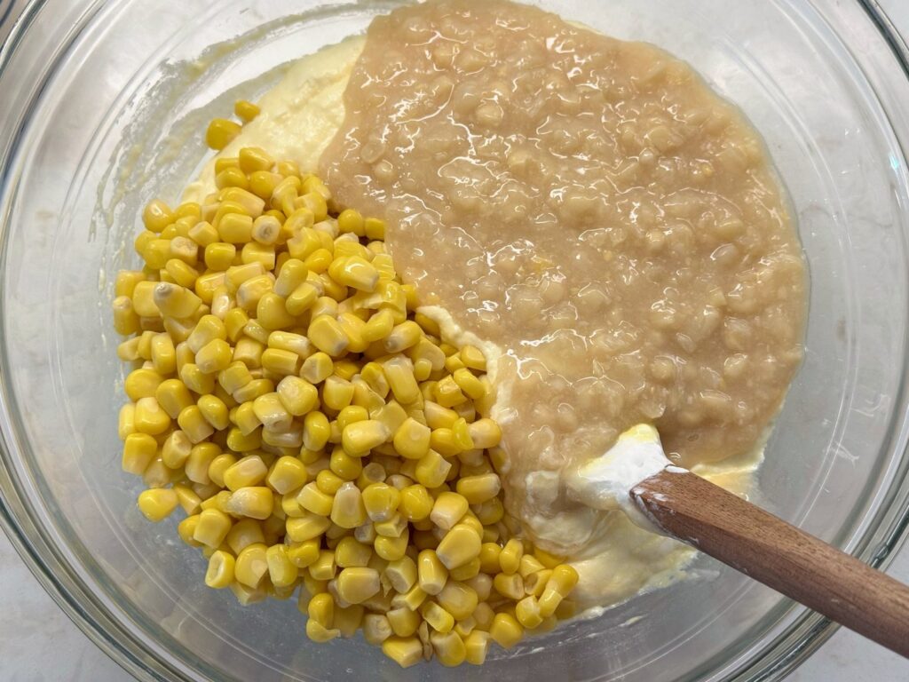 Drained whole kernel corn and cream-style corn added on top of the sour cream mixture in a glass bowl