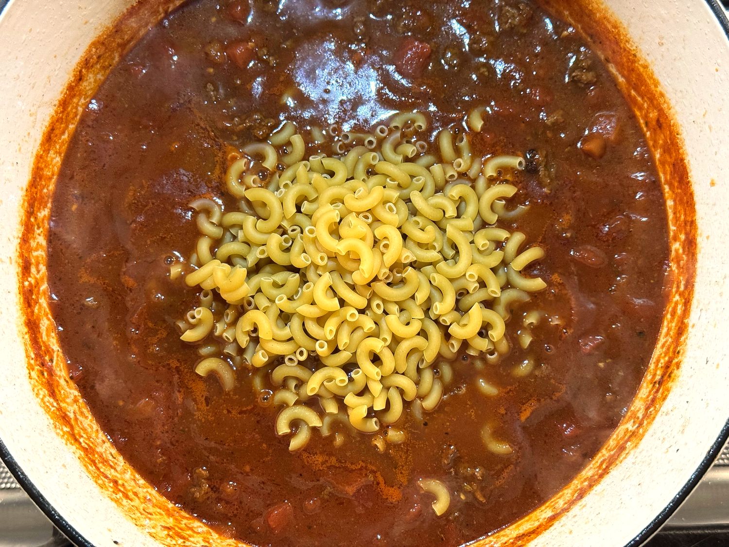Uncooked elbow macaroni added to the simmering tomato and venison sauce