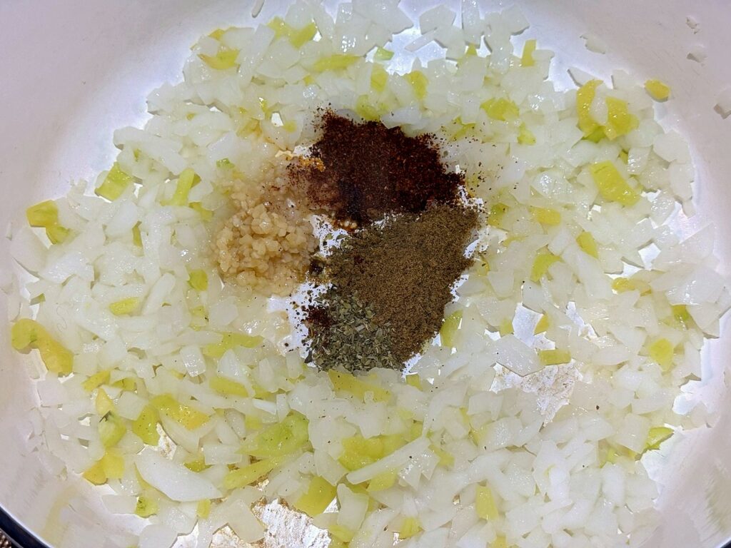 Minced garlic, cumin, oregano, and chili powder added on top of softened onion and peppers