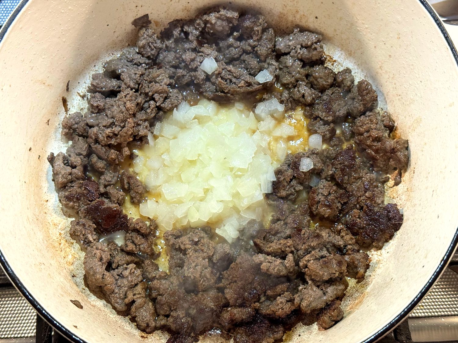 Diced onion added to a well in the center of browned ground venison in a Dutch oven