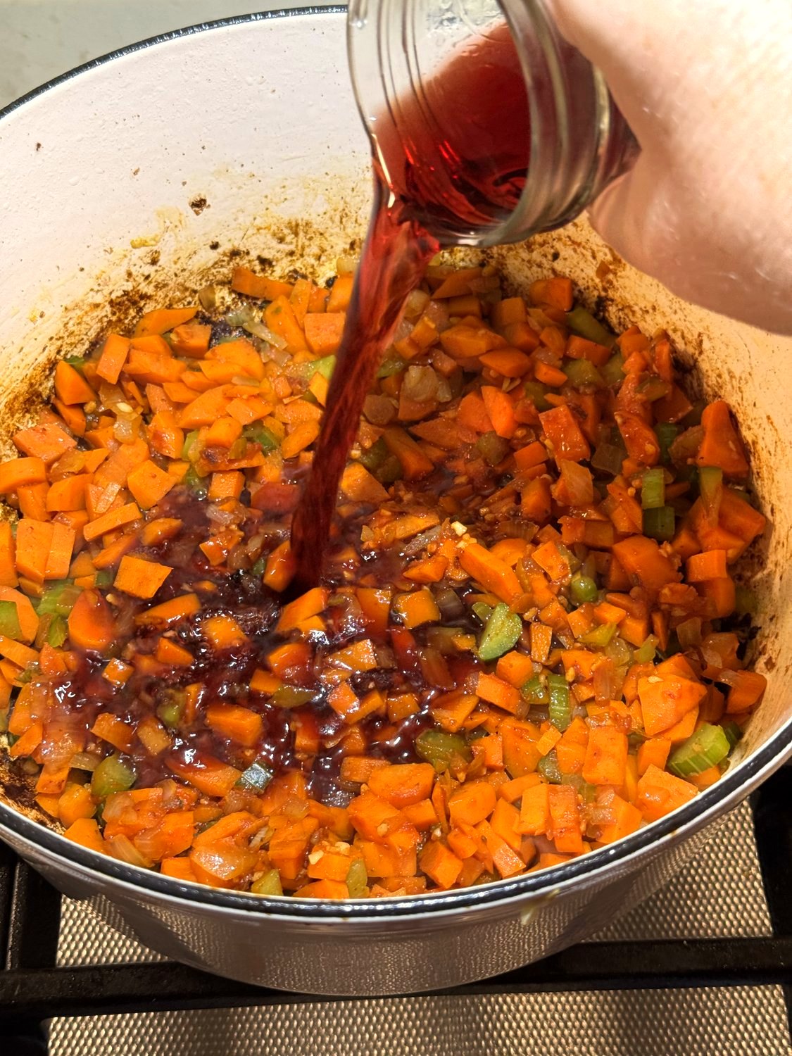 Red wine being poured from a jar into the vegetables in a Dutch oven