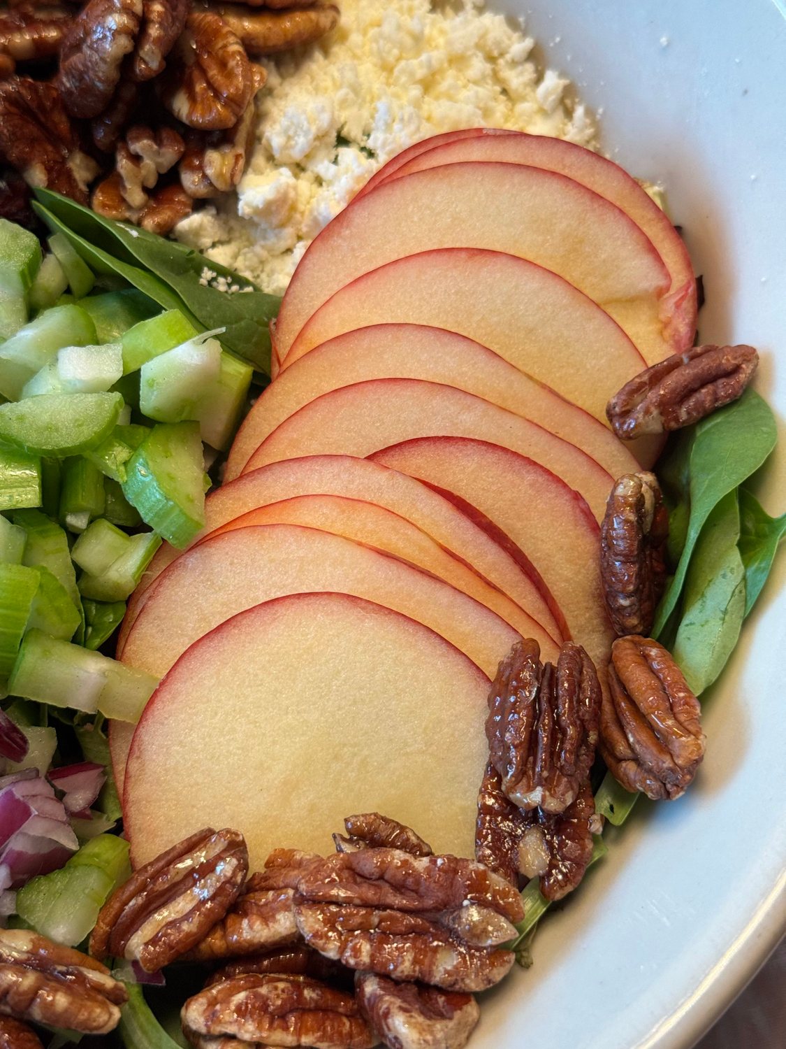 Close-up of thin Honeycrisp apple slices fanned over greens with maple pecans and feta