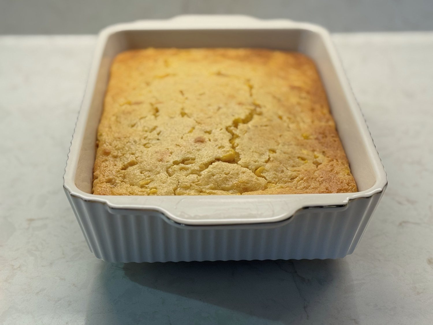 Front view of baked corn casserole in a white ribbed baking dish