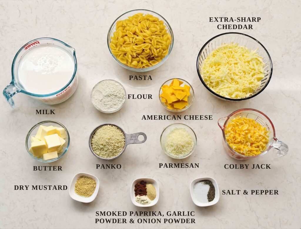 Labeled ingredients for baked mac and cheese: pasta shells, milk, extra-sharp cheddar, flour, American cheese, butter, panko, Parmesan, Colby Jack, dry mustard, smoked paprika, garlic powder, onion powder, salt, and pepper