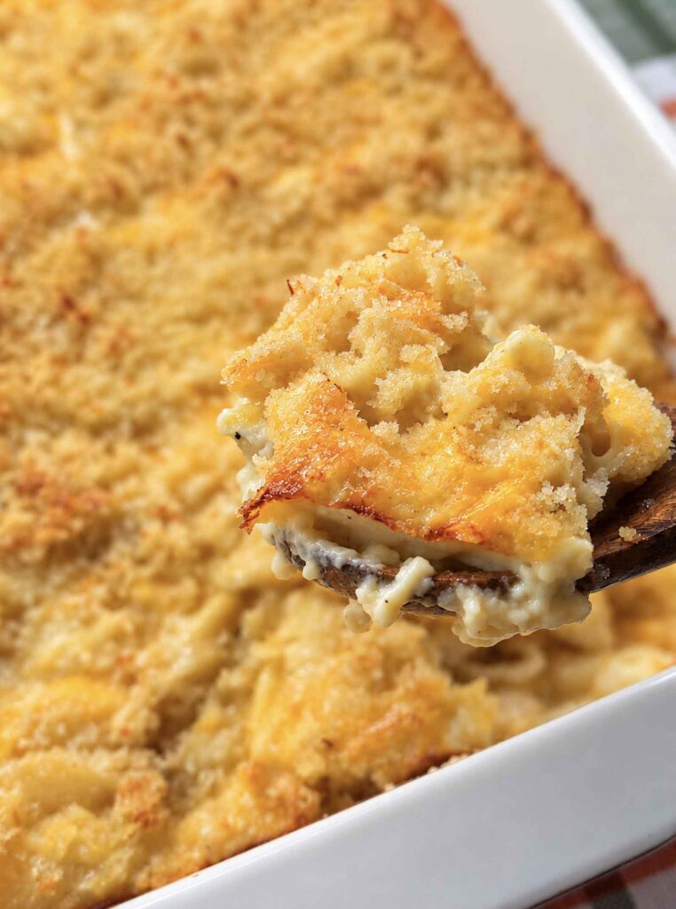 A wooden spoon lifting a scoop of baked mac and cheese with a crunchy golden crust and creamy shells underneath