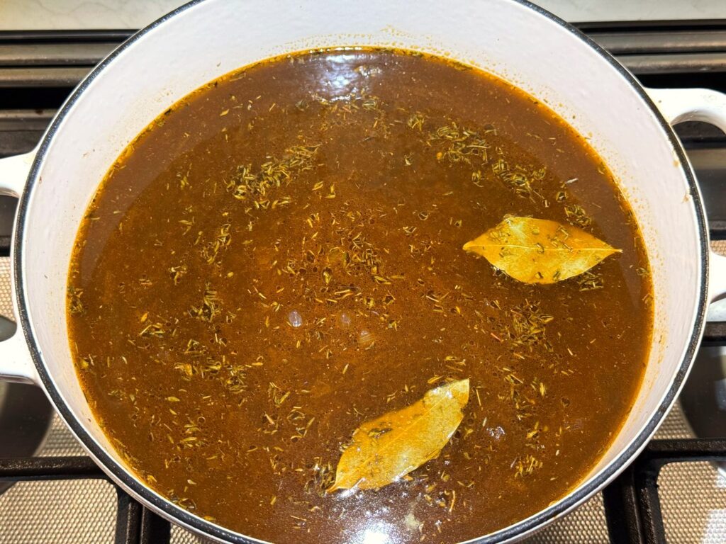 Bay leaves and dried thyme floating on the broth in a white Dutch oven