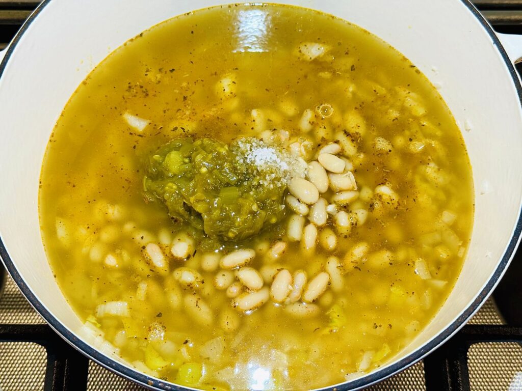 Whole great northern beans, diced green chiles, and salt added to the broth in a white Dutch oven