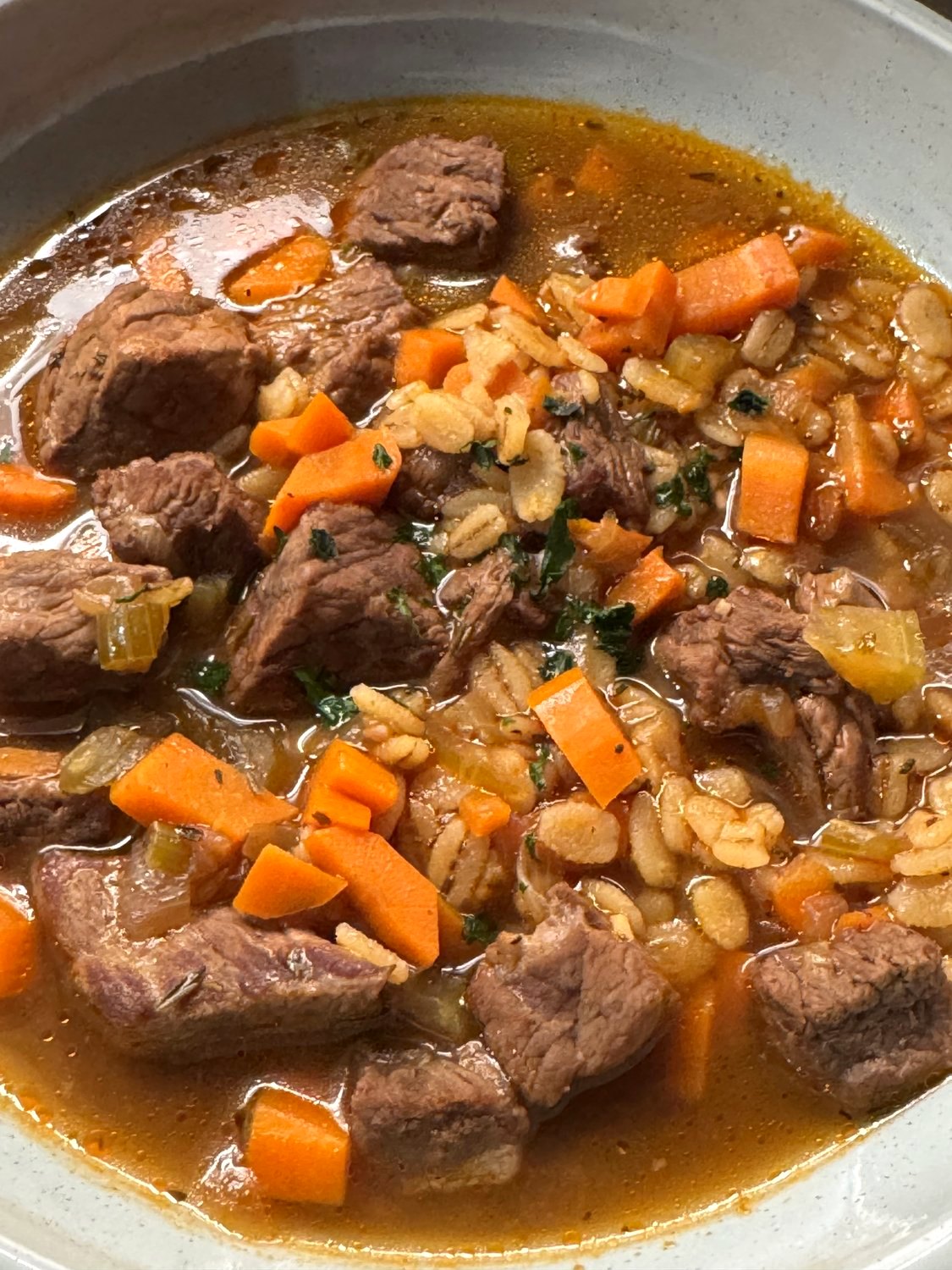 Close-up of beef barley soup with chunks of beef, carrots, celery, and barley in broth