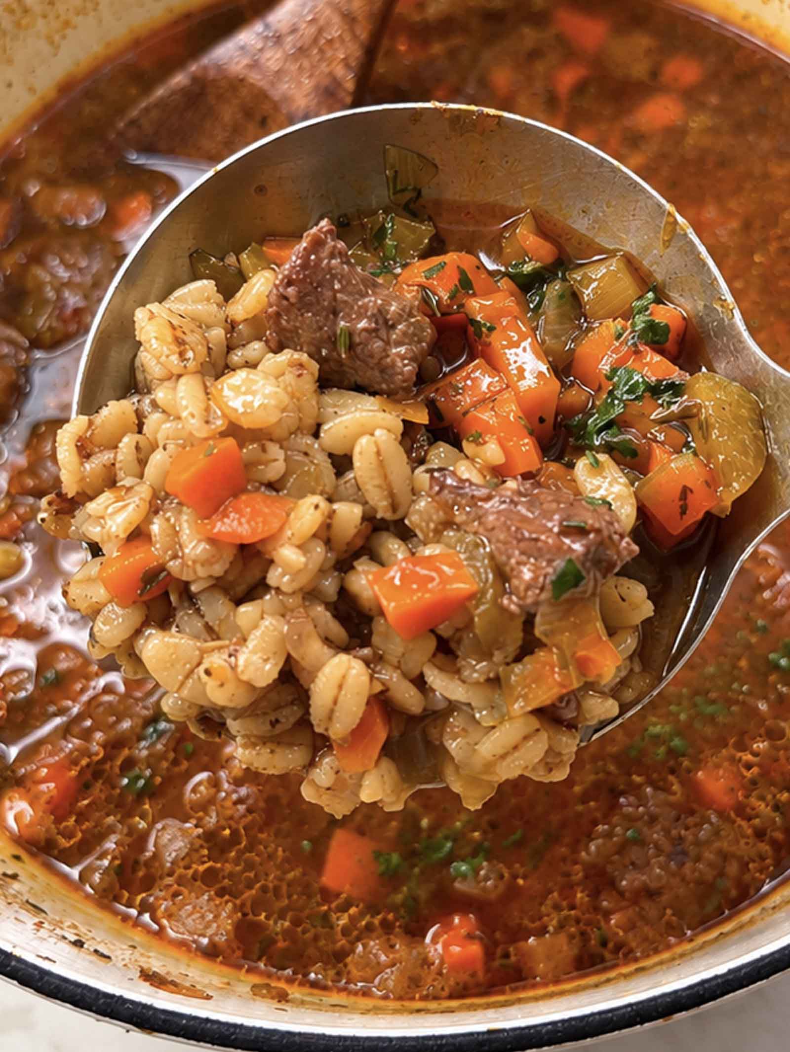 A ladle lifting beef barley soup out of a pot