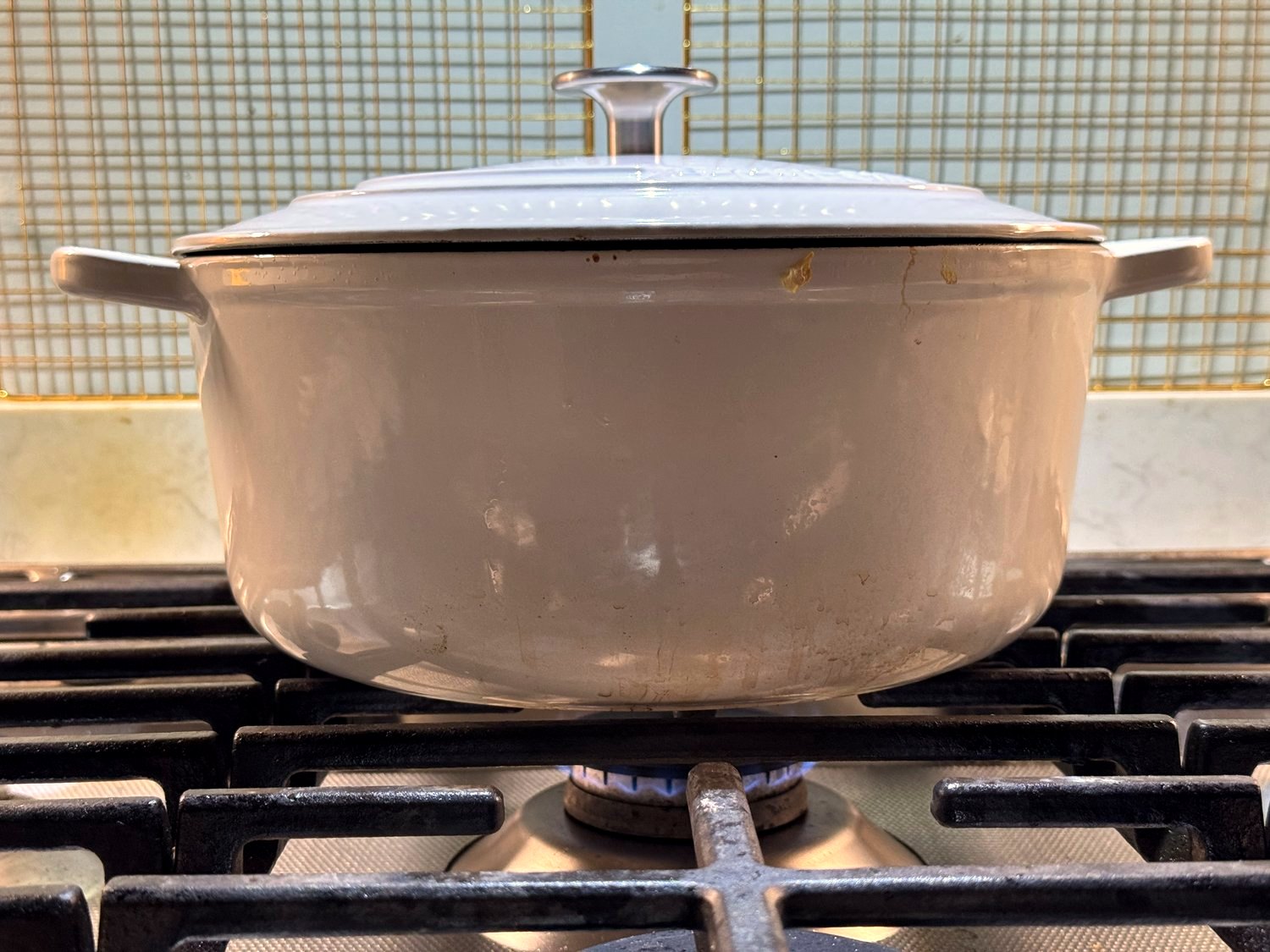 A covered white Dutch oven simmering on a gas stove