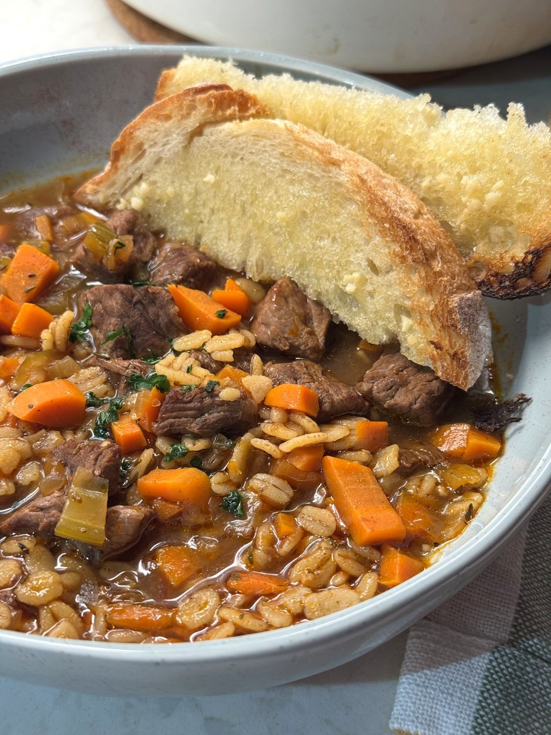 A bowl of beef barley soup with two thick slices of bread