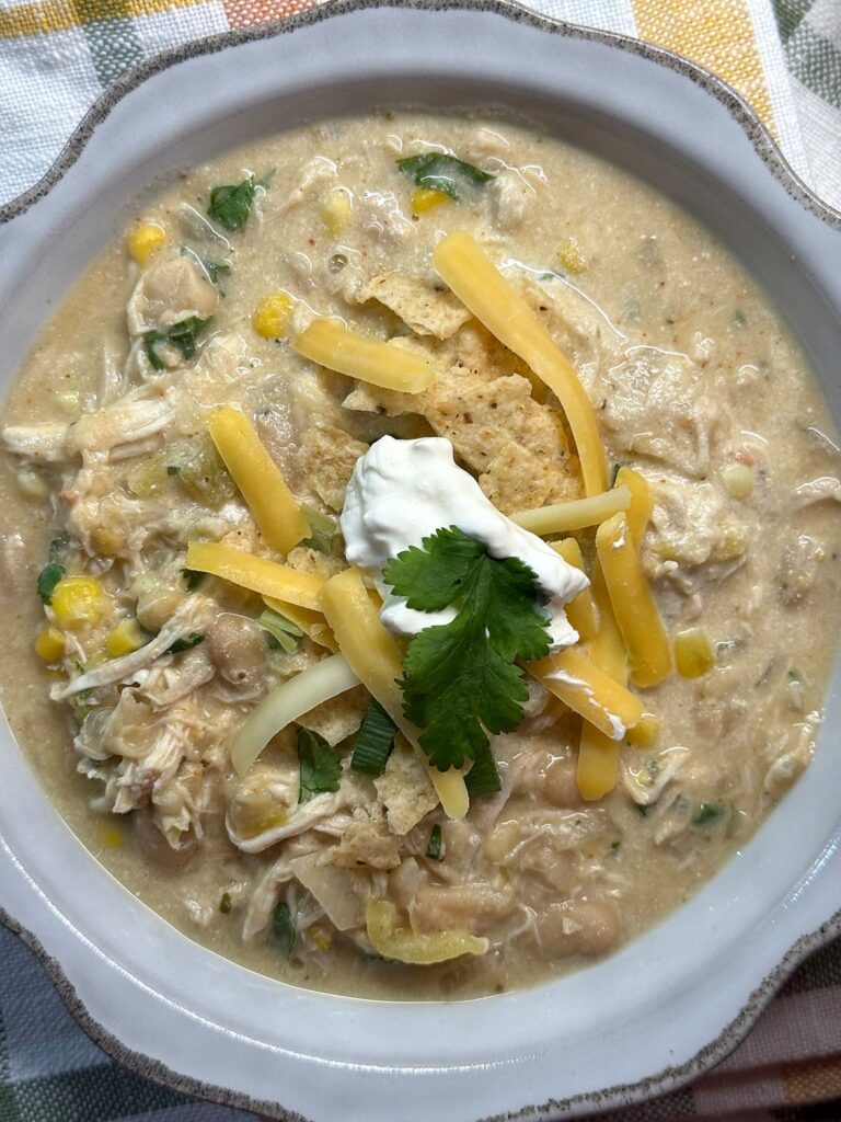 A gray bowl of white chicken chili topped with shredded cheddar, sour cream, and cilantro