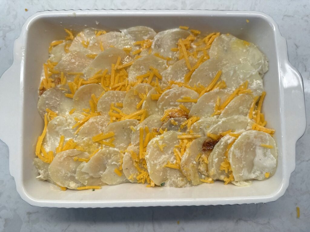 Shredded cheddar scattered along the seams between rows of shingled potato slices
