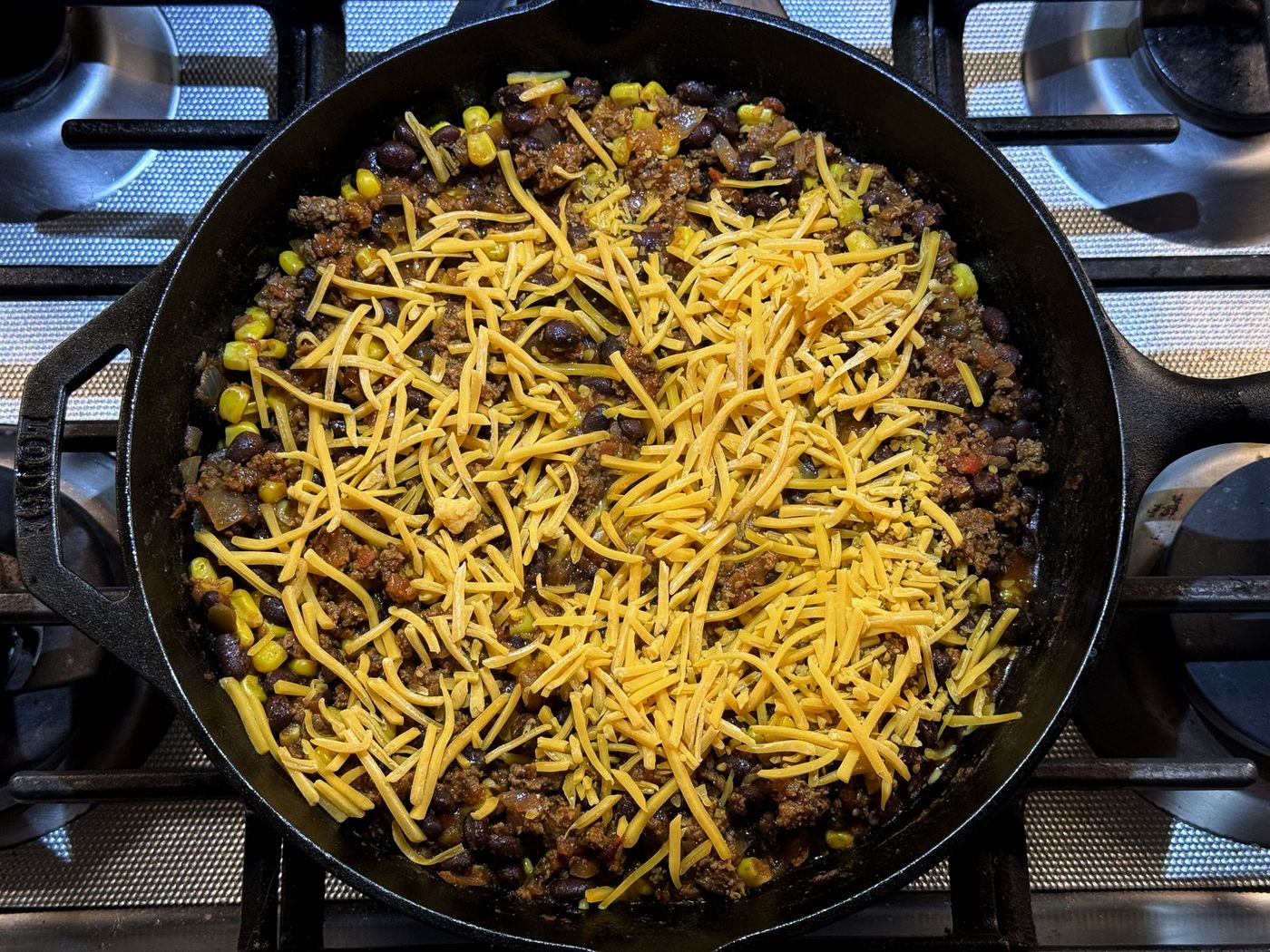 Shredded cheddar sprinkled over taco filling in a cast iron skillet before stirring