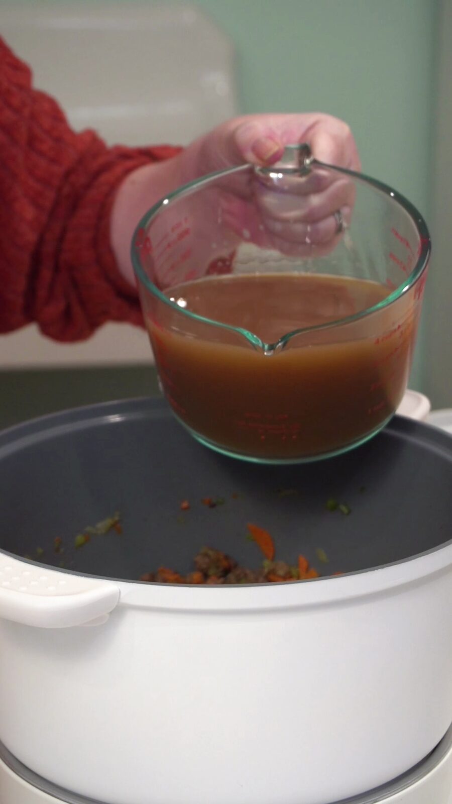 Pouring chicken broth from a glass measuring cup into the pot of beef and vegetables