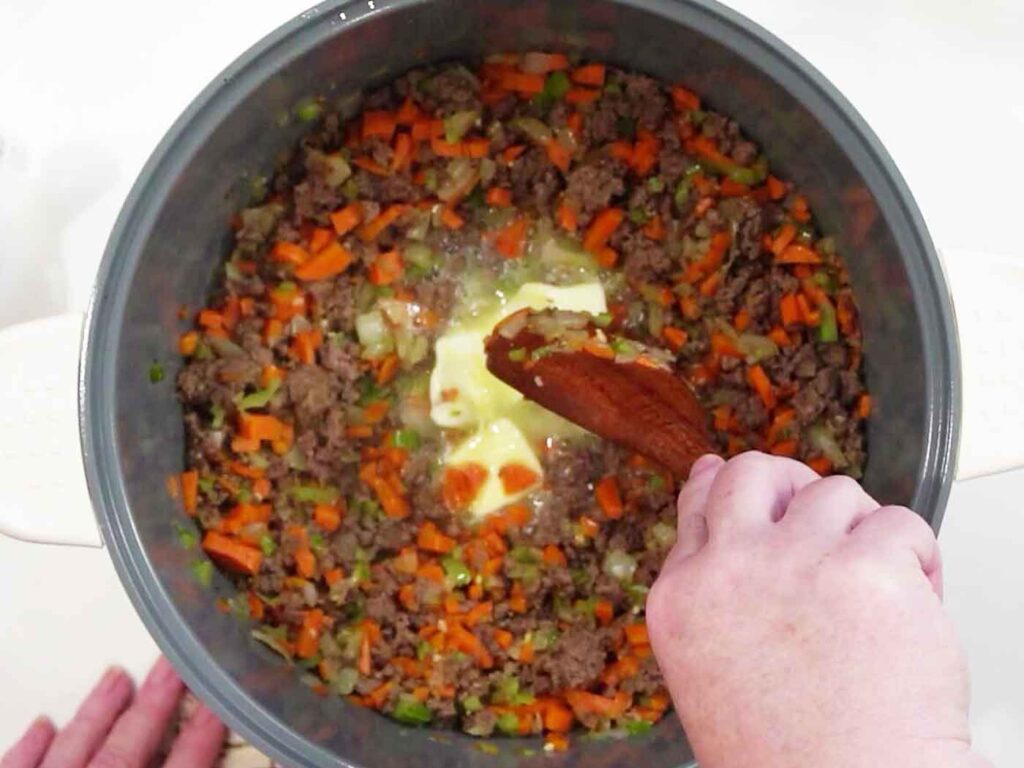 A pat of butter melting into ground beef and diced vegetables in a pot