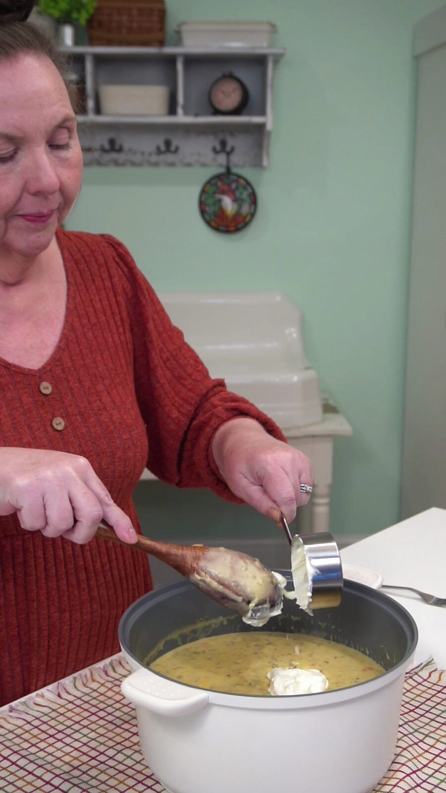Scraping sour cream from a measuring cup into the finished cheeseburger soup