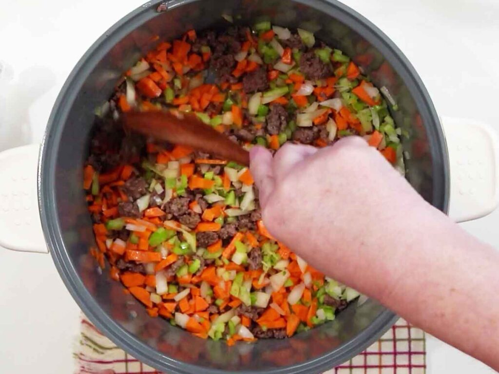 Diced onion, carrots, and celery added on top of browned ground beef in a pot