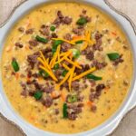 A bowl of hearty cheeseburger soup with ground beef, potatoes, carrots, cheese, and green onions