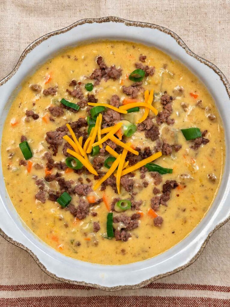 A bowl of hearty cheeseburger soup with ground beef, potatoes, carrots, cheese, and green onions