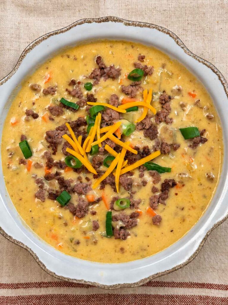 A bowl of hearty cheeseburger soup with ground beef, potatoes, carrots, cheese, and green onions