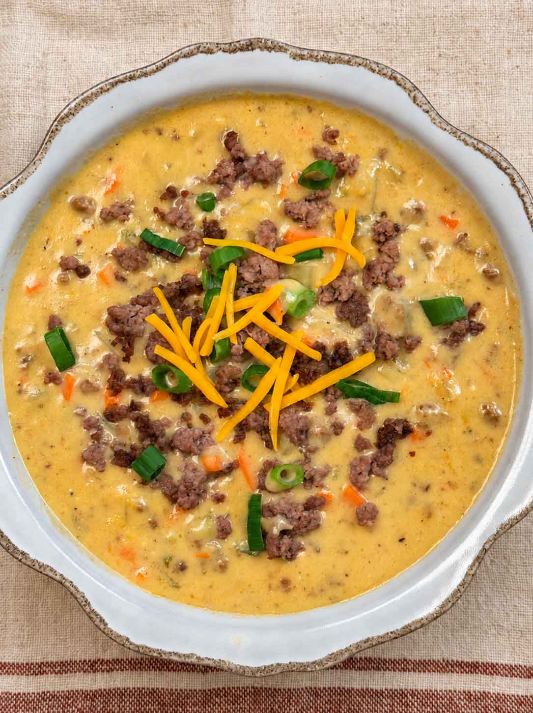 A bowl of hearty cheeseburger soup with ground beef, potatoes, carrots, cheese, and green onions