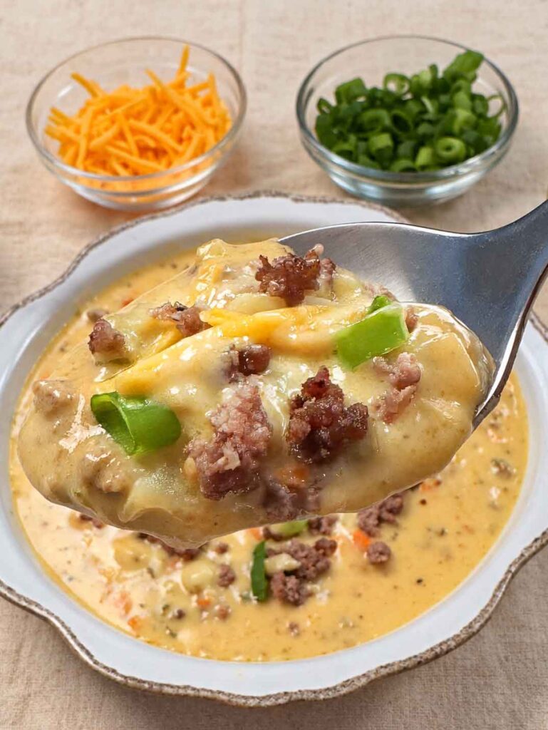 A spoonful of thick, creamy cheeseburger soup with ground beef, potato, cheddar, and green onion