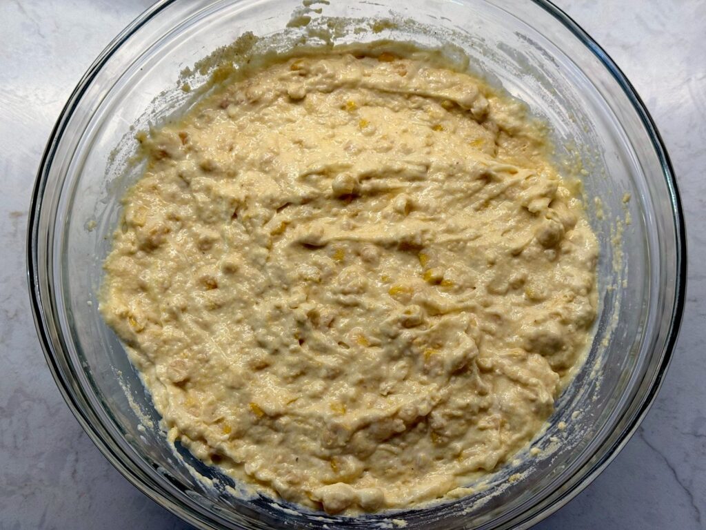 Thick corn casserole batter with Jiffy corn muffin mix stirred in, in a glass bowl