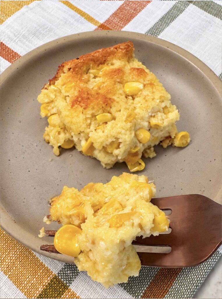 Closeup of a forkful of golden baked corn casserole on a tan plate