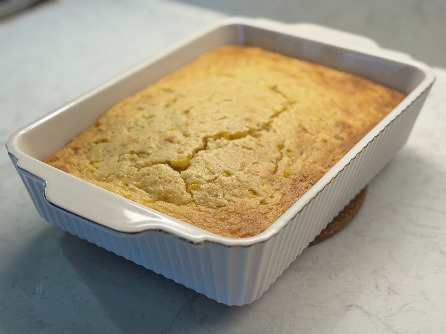 Baked corn casserole with a golden cracked top in a white ribbed baking dish