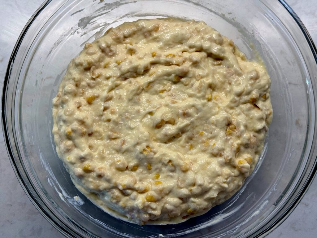 Corn, sour cream, butter, and eggs stirred together in a glass bowl