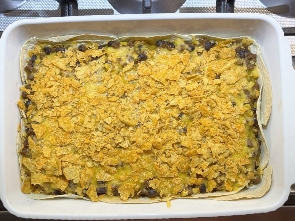 Crushed Doritos scattered over the melted cheese on a taco casserole before the last 5 minutes of baking