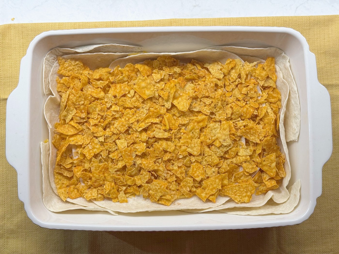 An even layer of crushed Nacho Cheese Doritos over the tortillas in a 9x13 baking dish