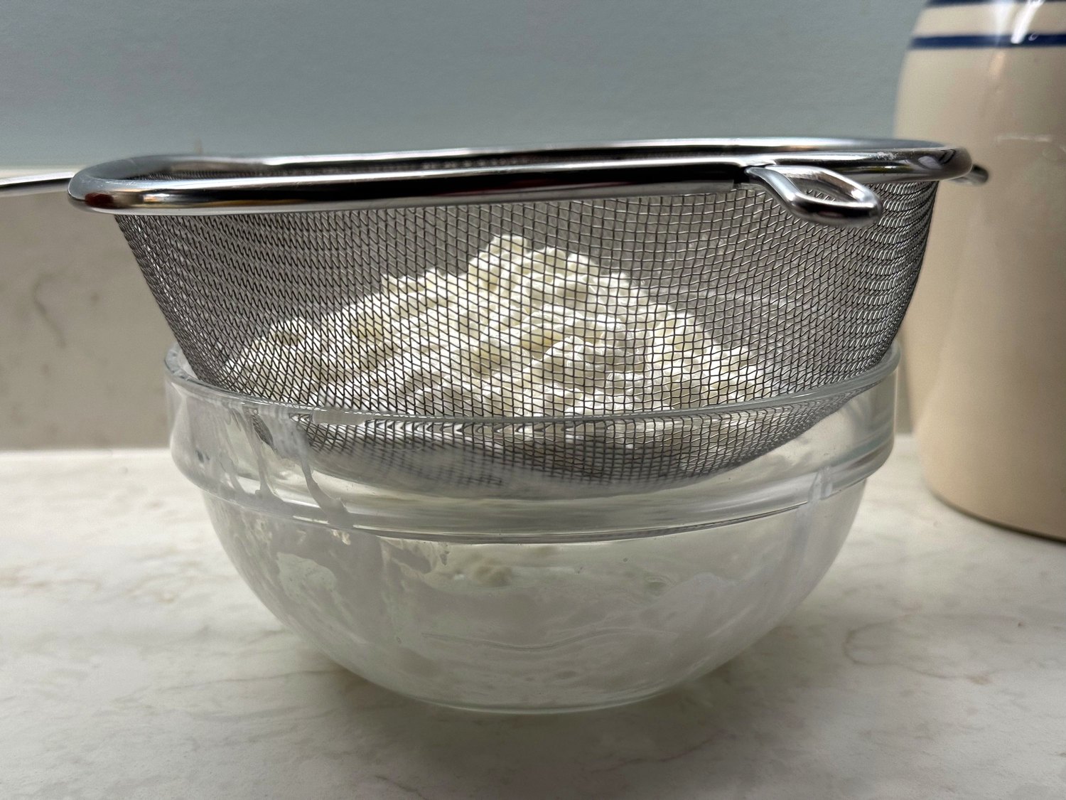 Cottage cheese draining in a fine-mesh strainer set over a glass bowl