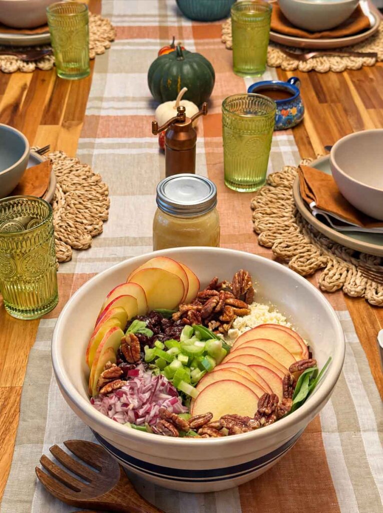 Fall harvest salad in a blue-striped bowl on a wooden dinner table set for fall with pumpkins and candles