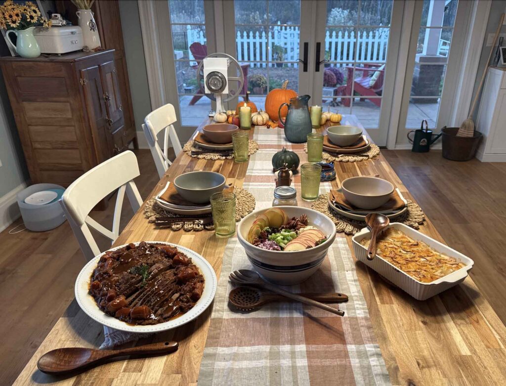 Autumn dinner table with fall salad, brisket, and scalloped potatoes with the table set for four and an antique ice box visible