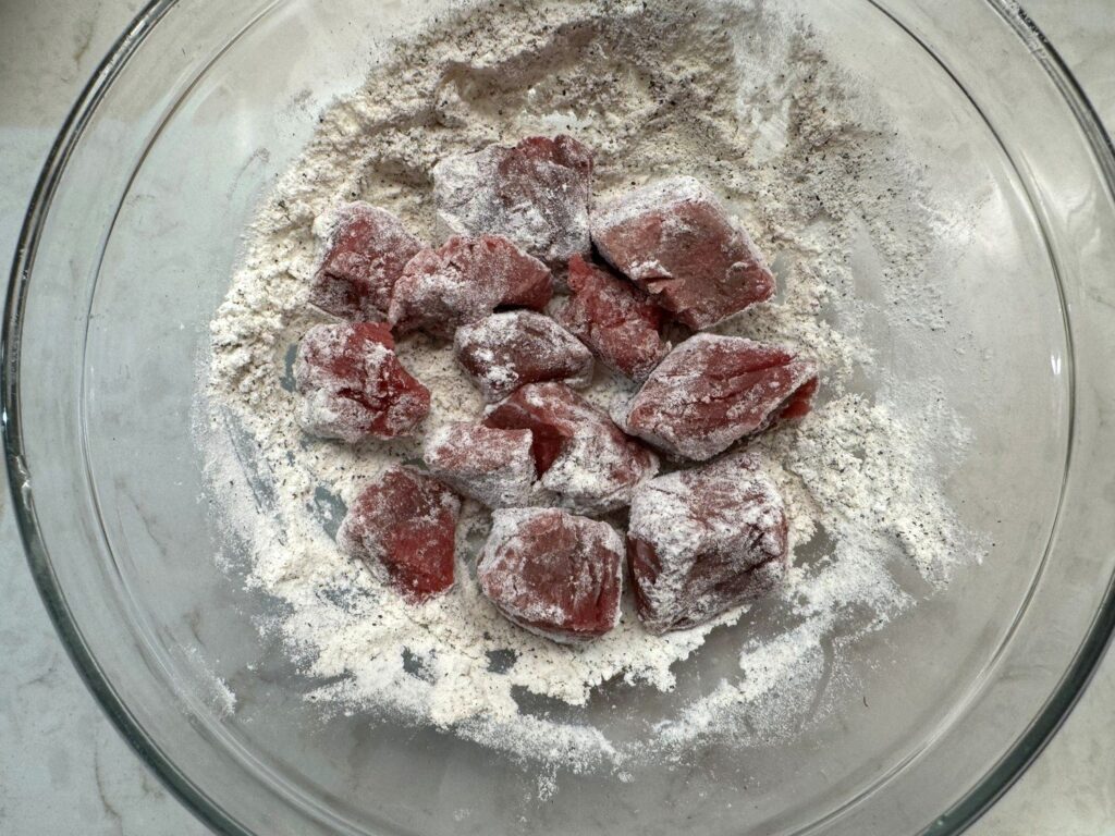 Cubes of beef stew meat tossed in flour in a glass bowl