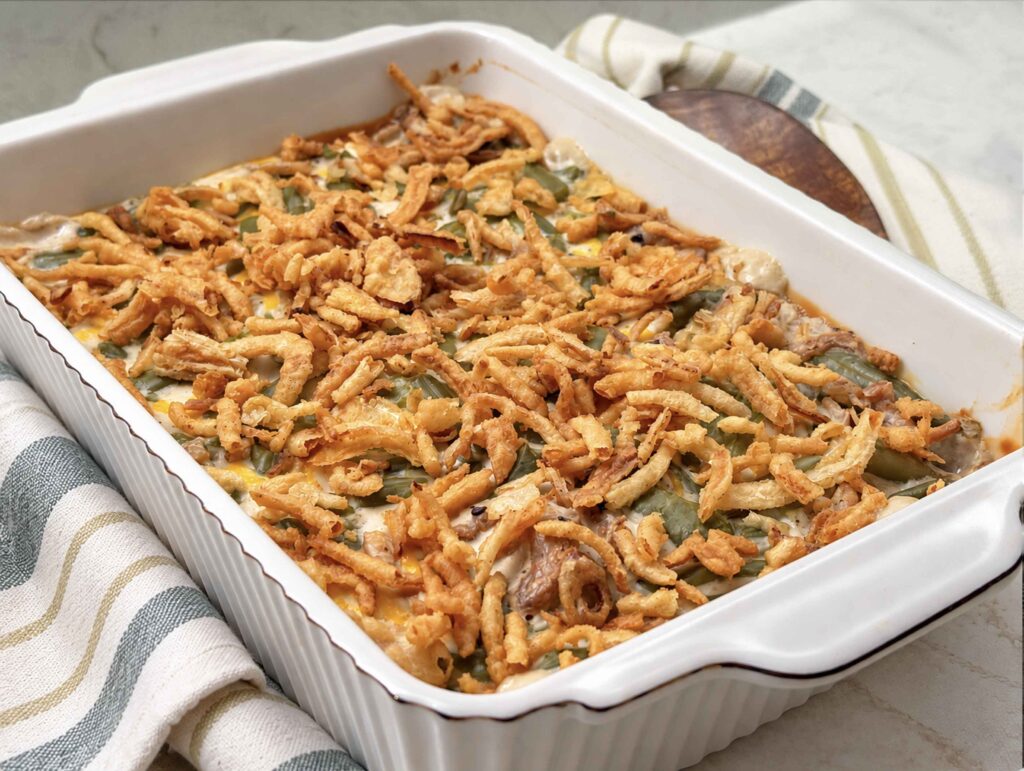 Classic green bean casserole with a golden fried onion topping in a white ruffled baking dish