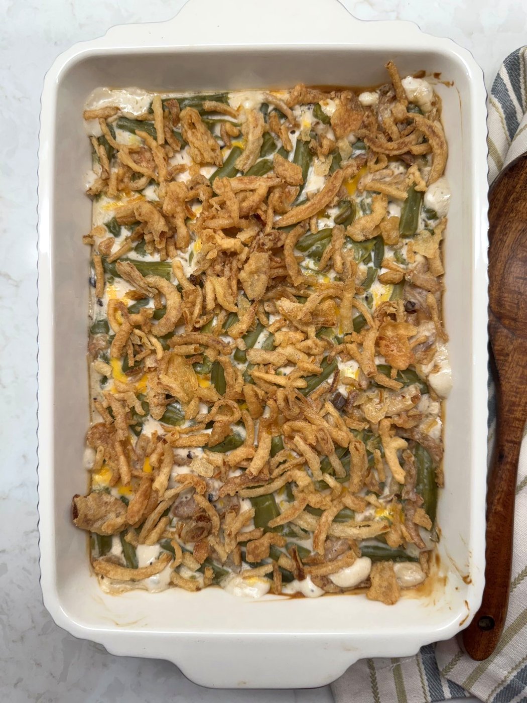 Overhead view of finished green bean casserole with golden brown fried onions in a white baking dish