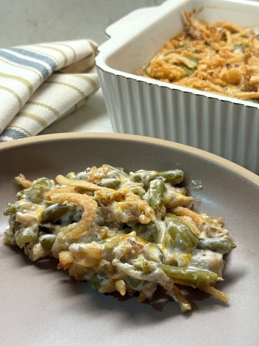 A serving of creamy green bean casserole on a plate in front of the baking dish
