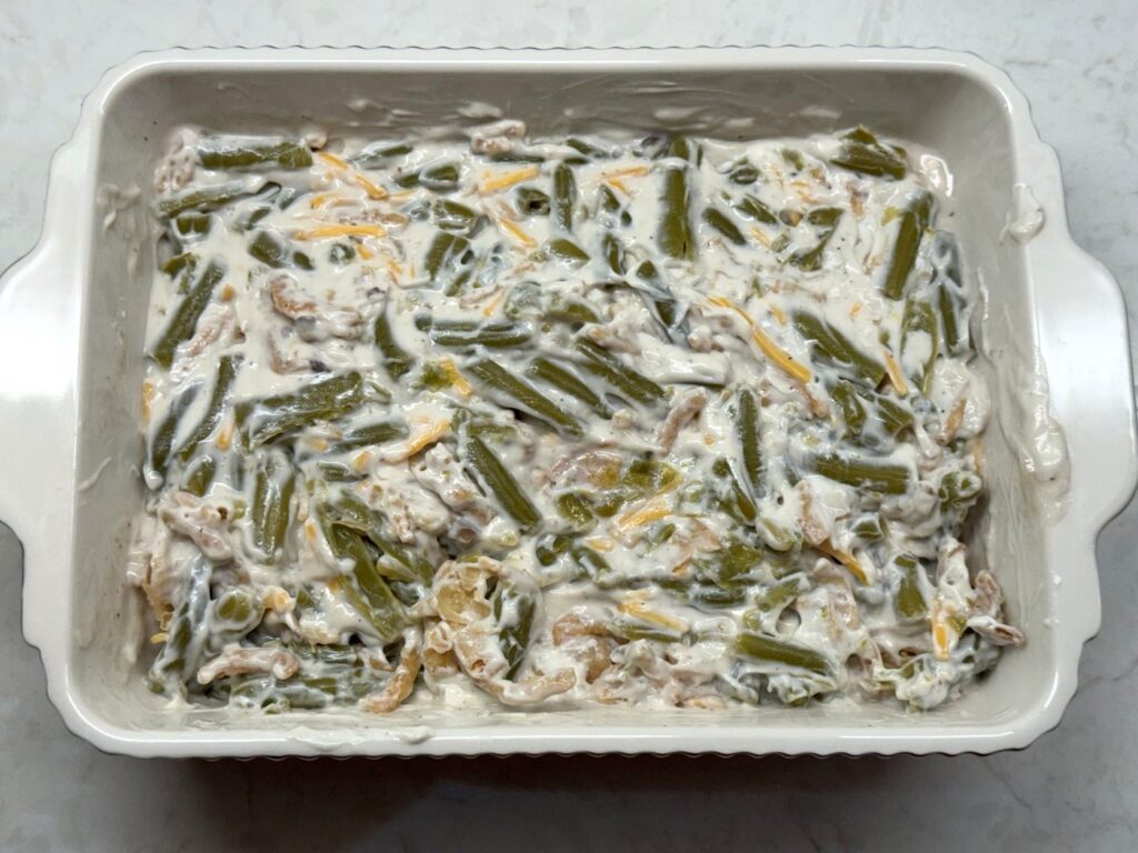 Green beans and fried onions folded into the creamy sauce, spread out in a white baking dish and ready to bake