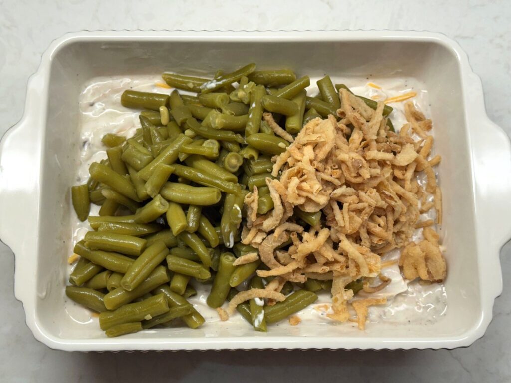 Drained green beans and fried onions added on top of the sauce in the baking dish