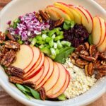 A bowl of salad with apples, feta cheese, maple pecans, red onions, celery and greens