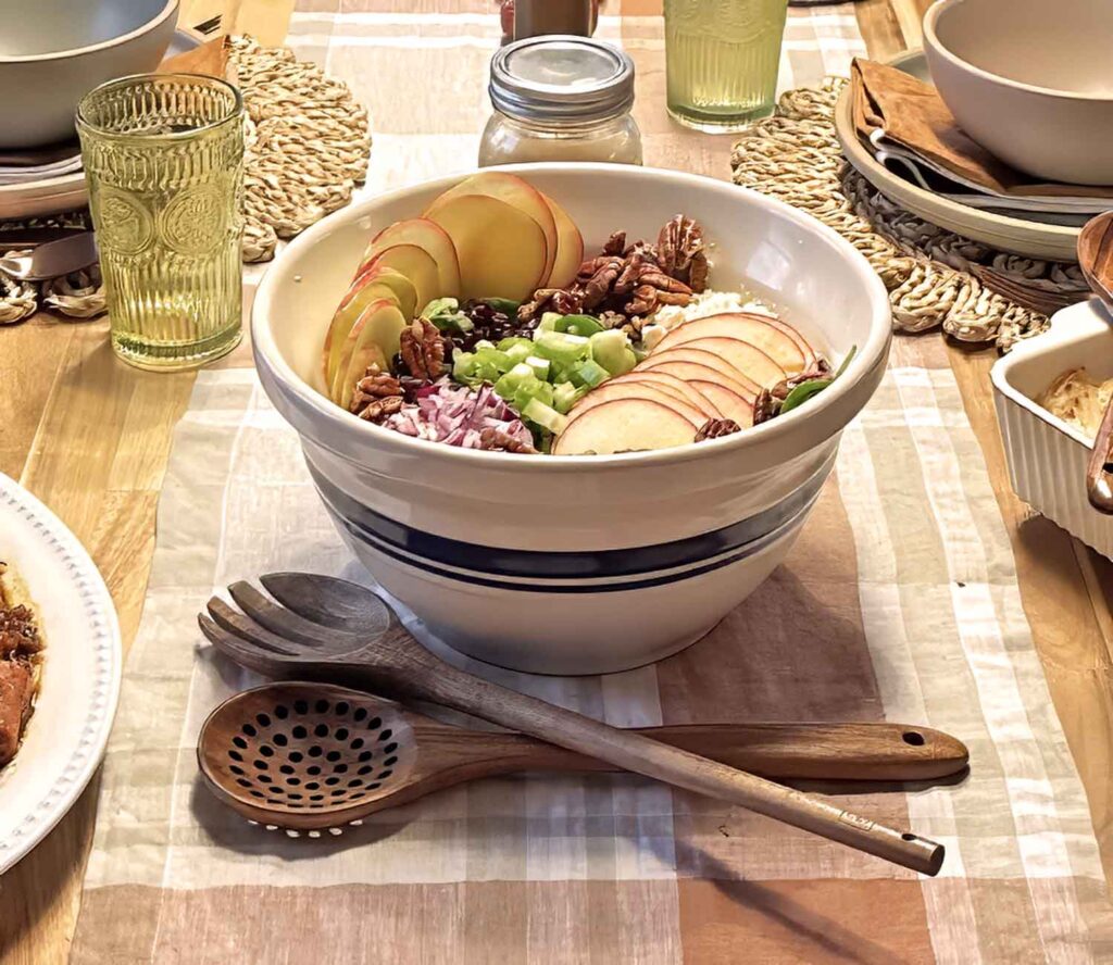 Fall harvest salad in a blue-striped bowl on a wooden dinner table set for fall with pumpkins and candles