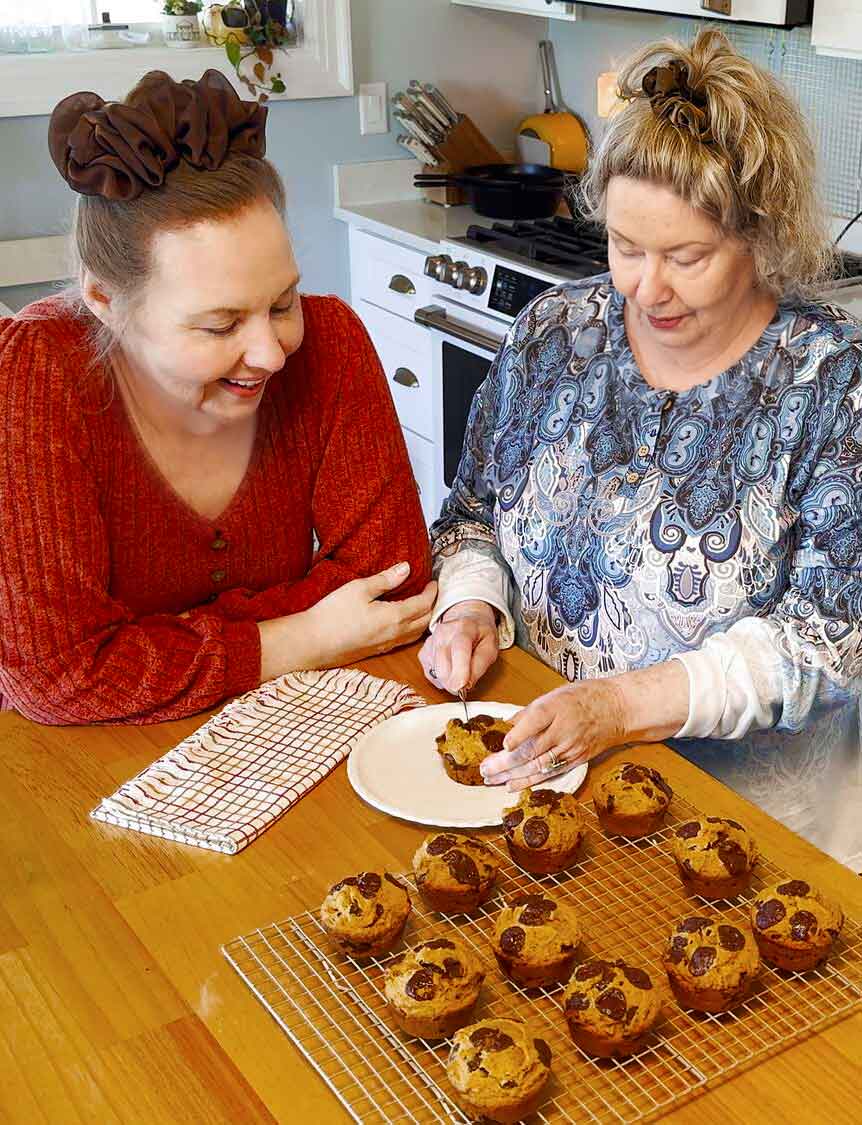 Jennifer Maker and her mom smiling over a plate of warm pumpkin chocolate chip muffins on a cooling rack