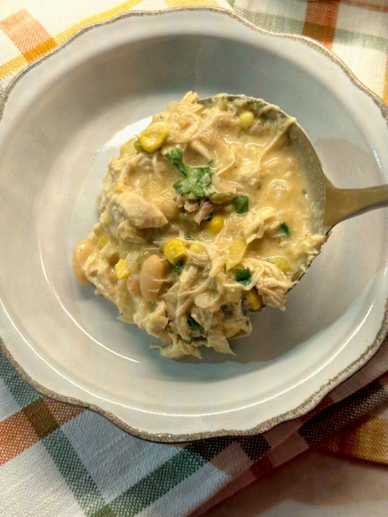 A ladle of white chicken chili being served into a gray bowl