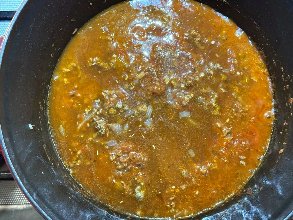 Beef broth added to the ground beef and spaghetti sauce in a Dutch oven