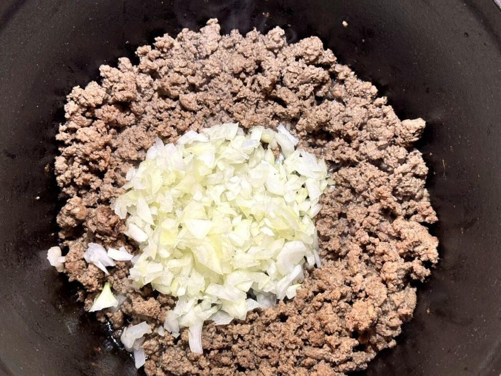 Diced onion added on top of cooked ground beef in a Dutch oven