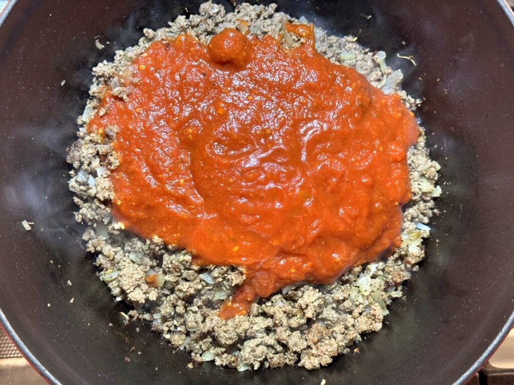 Spaghetti sauce poured over cooked ground beef and onion in a Dutch oven